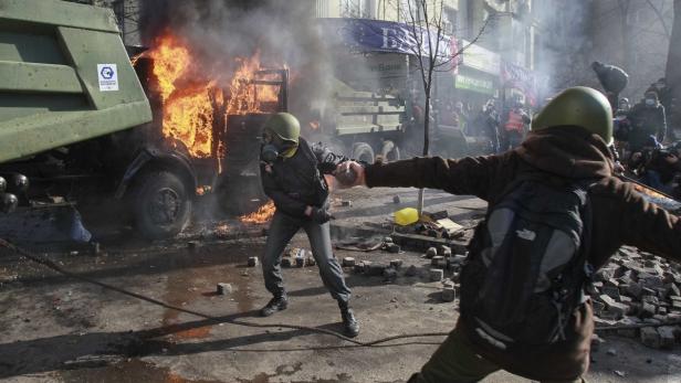 Bei einer Demonstration werfen Personen Steine auf einen brennenden Lastwagen.
