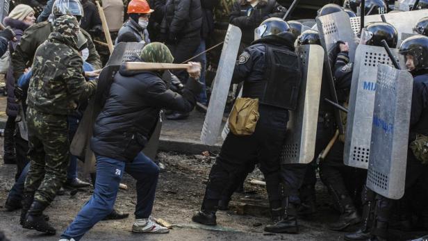 Ein Demonstrant schwingt einen Knüppel gegen eine Reihe von Polizisten mit Schutzschilden.