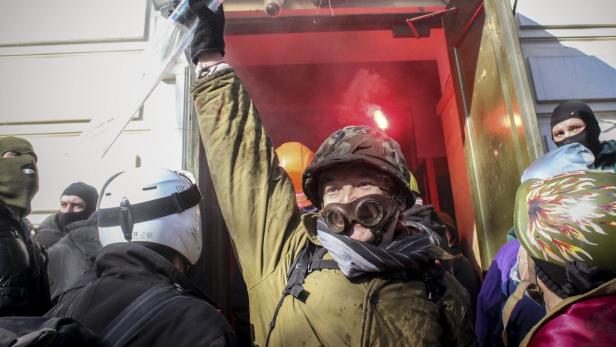 Eine Gruppe von Demonstranten, einige mit Sturmhauben und Helmen, vor einem Gebäude mit rotem Rauch.