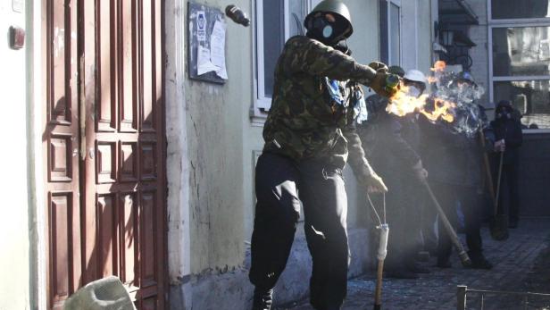 Eine Gruppe von Personen mit Gasmasken und Fackeln steht vor einem Gebäude.