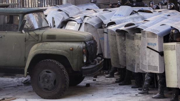 Eine Reihe von Polizisten mit Schutzschilden steht vor einem olivgrünen Lastwagen.