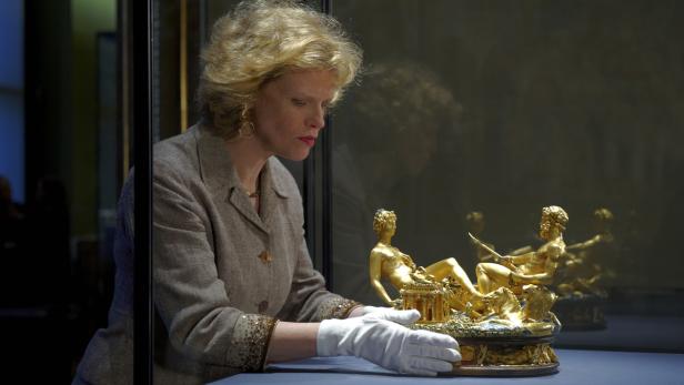 Eine Frau mit Handschuhen betrachtet eine goldene Skulptur in einer Vitrine.