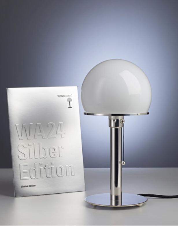 Die „WA24 Silber Edition“ Tischleuchte von Tecnolumen mit einer Broschüre im Hintergrund.