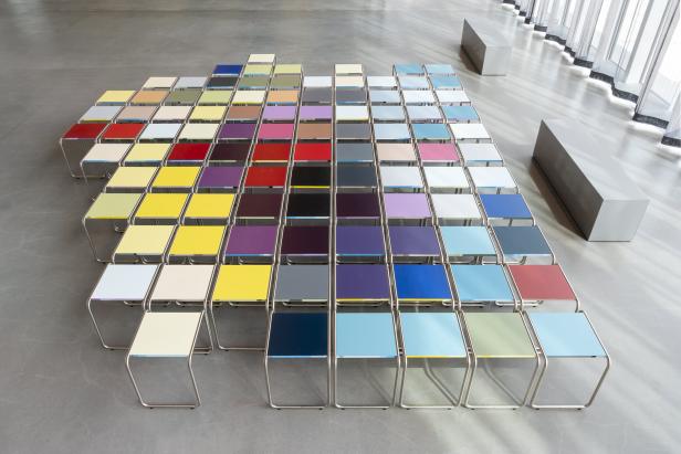 Eine Anordnung von kleinen, bunten Tischen in einem Ausstellungsraum.