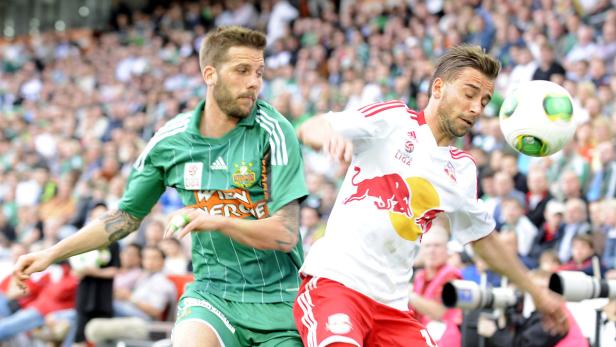 Zwei Fußballspieler kämpfen vor einer Zuschauermenge um den Ball.