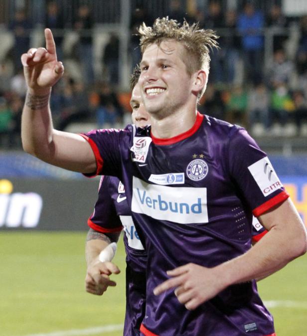 Ein jubelnder Fußballspieler in lila Trikot zeigt mit dem Finger nach oben.