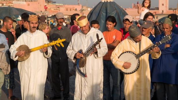 Eine Gruppe marokkanischer Musiker spielt traditionelle Instrumente auf einem belebten Platz.