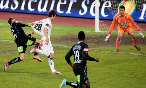 Ein Fußballspieler zieht am Trikot eines Gegenspielers, während der Torwart zusieht.