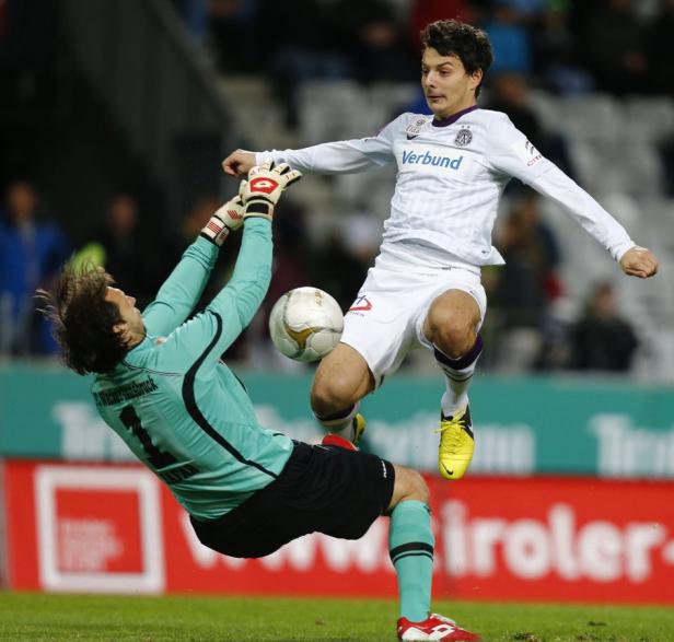Ein Fußballspieler springt, um den Ball zu treten, während der Torwart versucht, ihn abzuwehren.