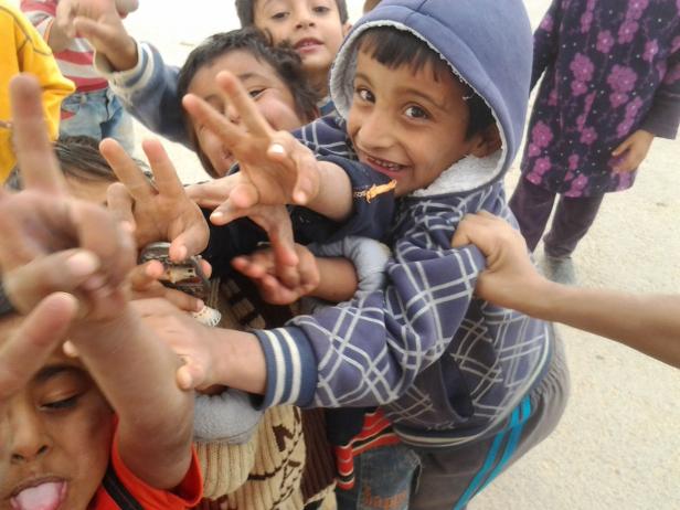 Eine Gruppe Kinder drängt sich um die Kamera und formt mit ihren Händen Victory-Zeichen.