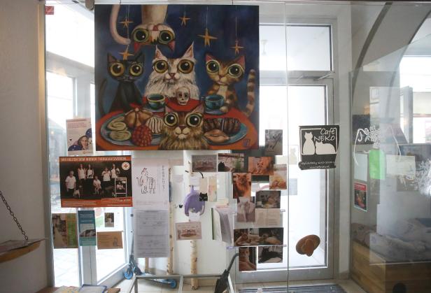 Ein Schaufenster des „Café Neko“ mit Katzenbildern und einem Katzenkunstwerk.