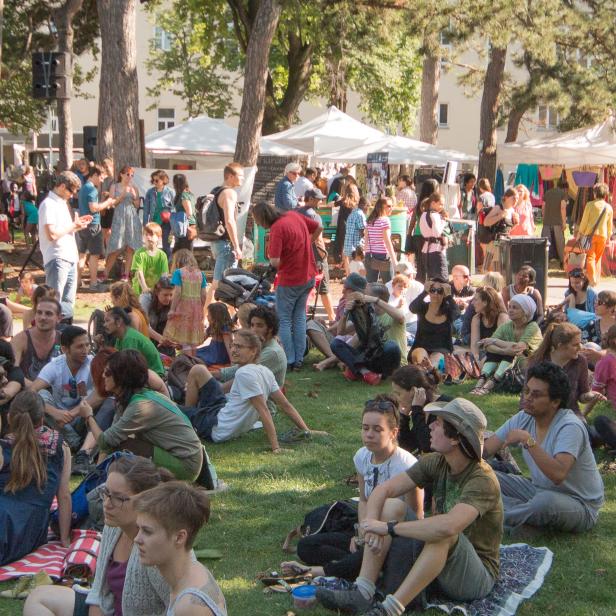 Viele Menschen sitzen und stehen auf einer Wiese bei einem Markt.
