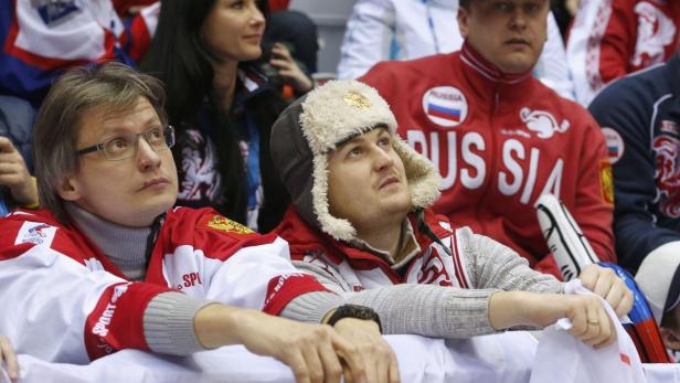 Zuschauer in russischen Sportjacken und einer Pelzmütze schauen aufmerksam zu.