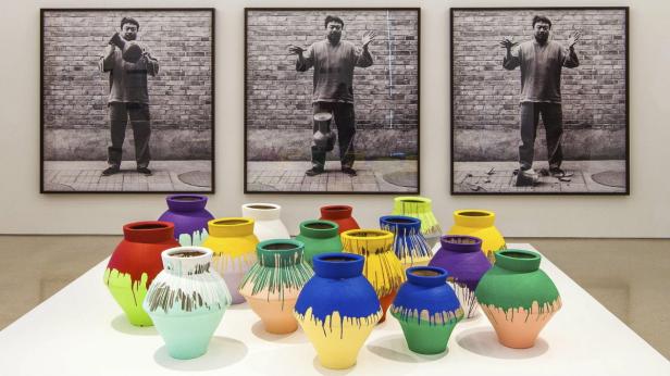 Eine Ausstellung mit farbig bemalten Vasen vor drei Schwarzweißfotografien von Ai Weiwei.
