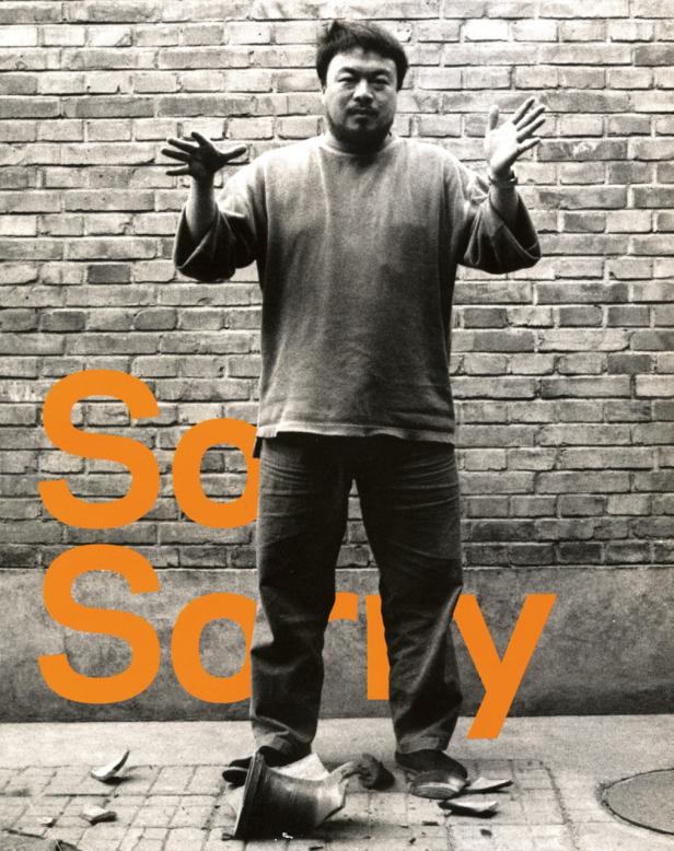 Ein Mann steht vor einer Ziegelmauer mit erhobenen Händen, neben einer zerbrochenen Vase.