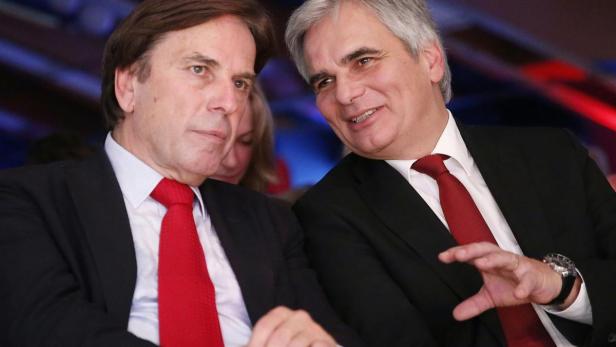 Zwei Männer in Anzügen mit roten Krawatten unterhalten sich.