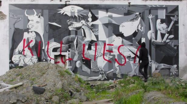 Eine Person sprüht rote Farbe auf ein großes Wandgemälde im Stil von Picassos „Guernica“.