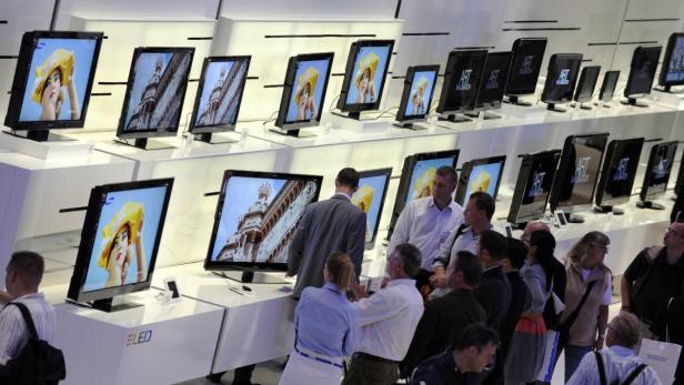 Eine Gruppe von Menschen betrachtet Fernseher auf einem Messestand.