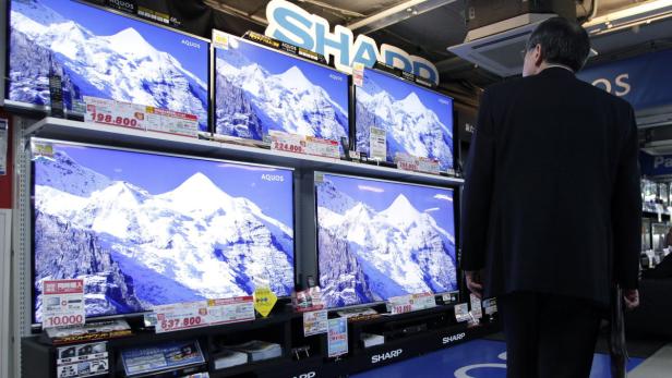 Ein Mann betrachtet in einem Geschäft eine Reihe von Sharp Aquos Fernsehern, die Berglandschaften zeigen.