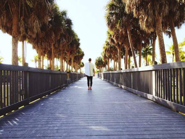 Ein Mann geht auf einem Holzsteg entlang, gesäumt von Palmen.