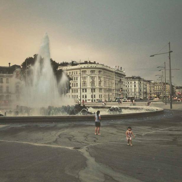 Ein Brunnen sprüht Wasser in die Luft, während eine Frau und ein Kind davor stehen.