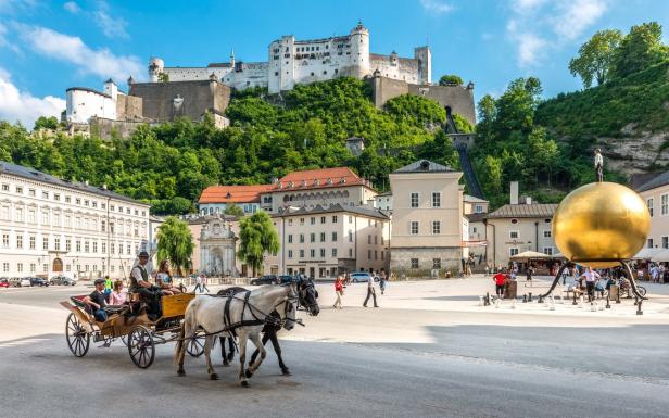 Pferdekutsche fährt über den Residenzplatz in Salzburg, im Hintergrund die Festung Hohensalzburg.