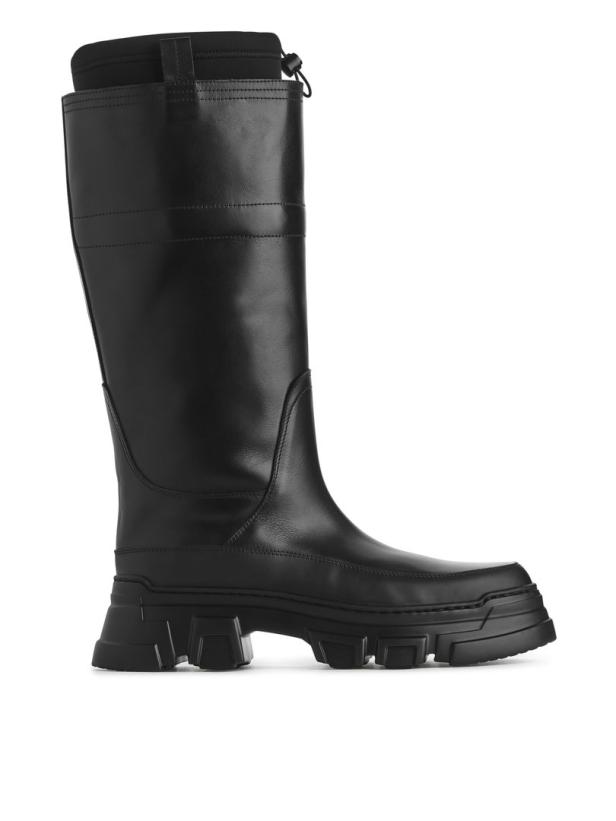 Ein einzelner, hoher, schwarzer Stiefel mit dicker Sohle steht auf einem weißen Hintergrund.