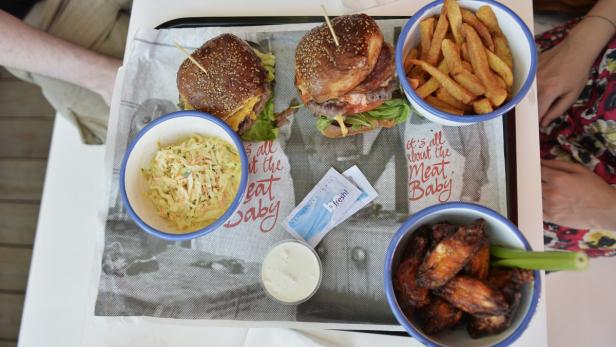 Zwei Burger, Pommes, Krautsalat und Chicken Wings auf einem Tablett.