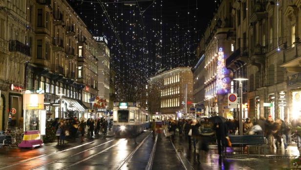 Eine belebte Straße in Zürich ist weihnachtlich geschmückt und von einem Zug befahren.