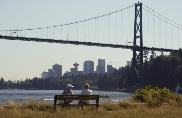 Zwei Personen sitzen auf einer Bank mit Blick auf die Lions Gate Bridge und die Skyline von Vancouver.