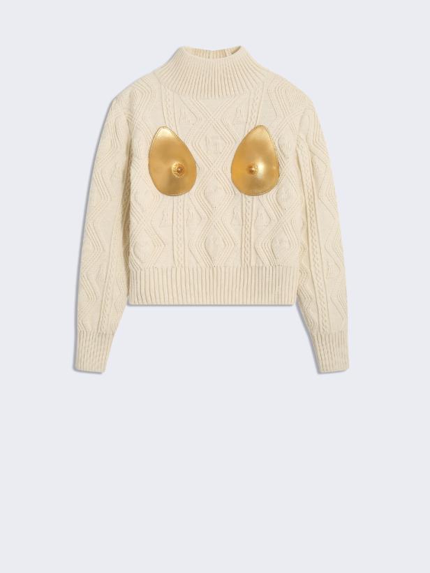 Ein cremefarbener Strickpullover mit goldenen Applikationen in Form stilisierter Brüste.