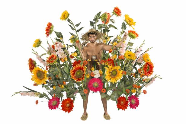 Ein Mann mit Strohhut und Blumen geschmückt vor einem weißen Hintergrund.