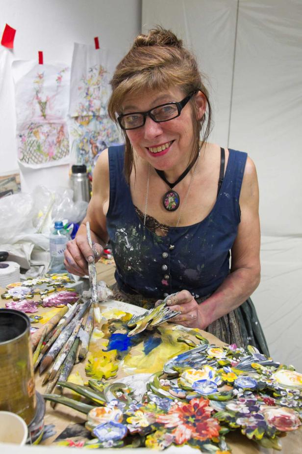 Eine lächelnde Künstlerin bemalt hölzerne Blumen in ihrem Atelier.