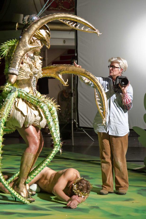 Eine Fotografin inszeniert eine Szene mit einer Person im Insektenkostüm und einer weiteren am Boden liegenden Person.