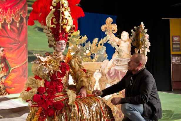 Eine Frau in einem aufwendigen, goldenen Kostüm mit roten Akzenten und Federn, neben einem Mann in Jeans.