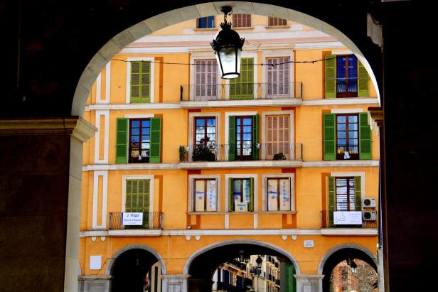 Ein gelbes Gebäude mit Fensterläden, gesehen durch einen Torbogen auf der Plaça Major.