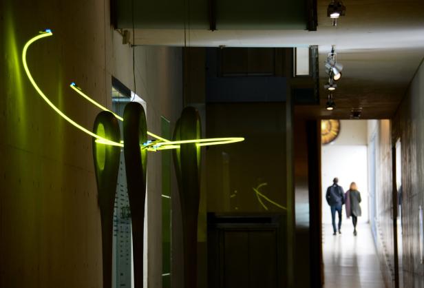 Eine Installation mit überdimensionalen Nadeln und leuchtenden Fäden in einem Museumsgang.