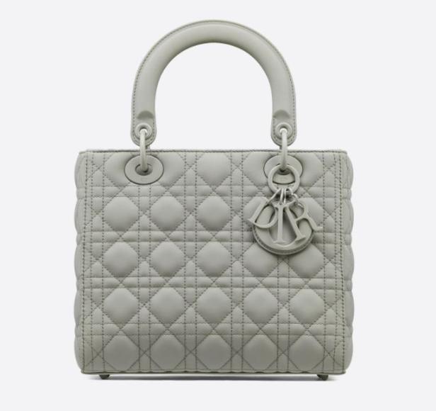 Eine graue, gesteppte Lady Dior Handtasche mit silbernen Anhängern vor einem weißen Hintergrund.