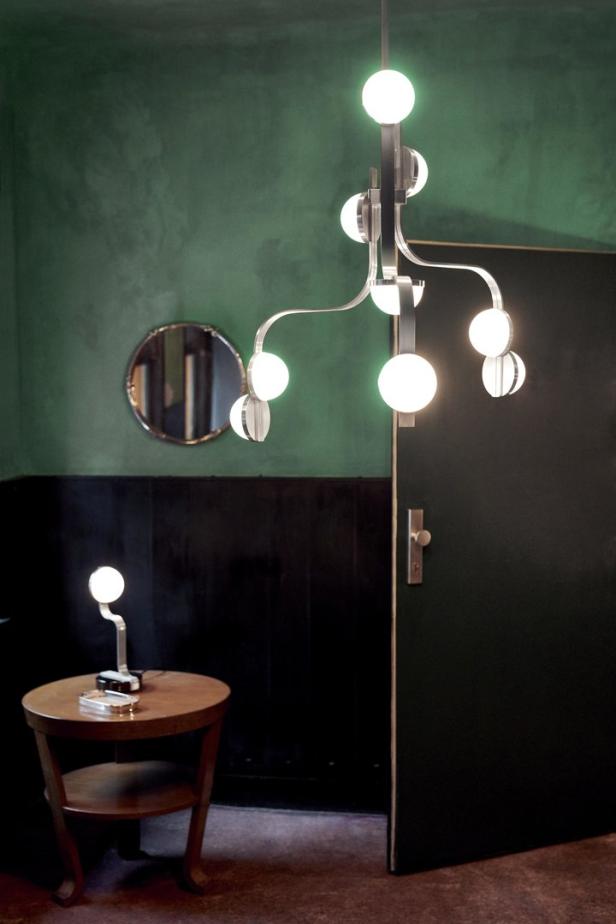 Eine moderne Lampe mit kugelförmigen Leuchten hängt in einem Raum mit grünen Wänden.