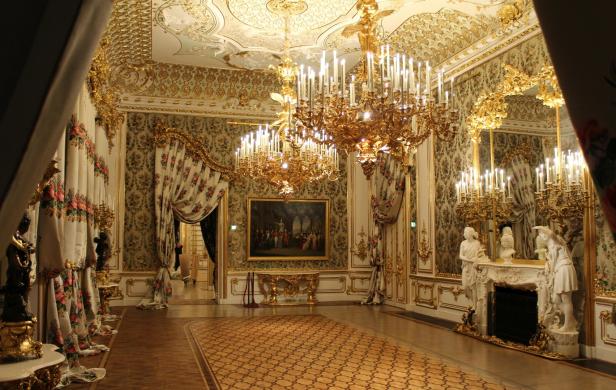 Ein prunkvoller Saal mit goldenen Verzierungen, Kristalllüstern und floralen Vorhängen.