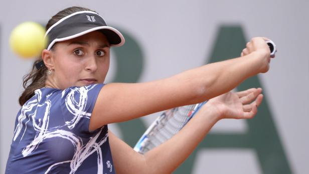 Eine Tennisspielerin schlägt einen gelben Ball mit ihrem Schläger.