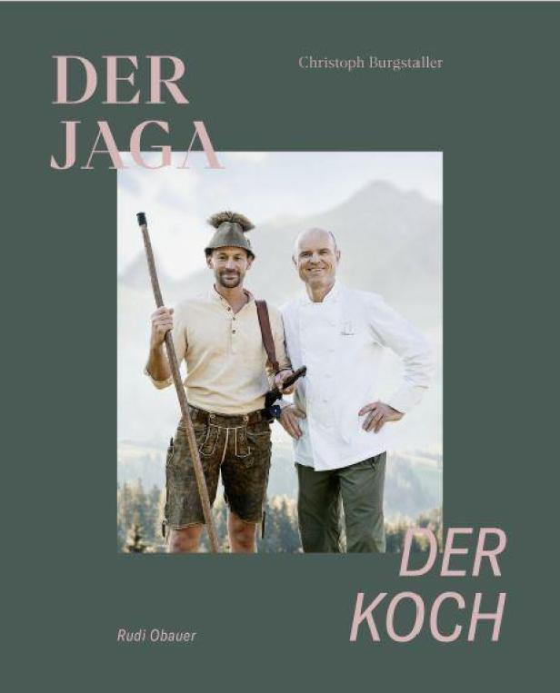 Ein Koch und ein Jäger stehen vor einer Bergkulisse.