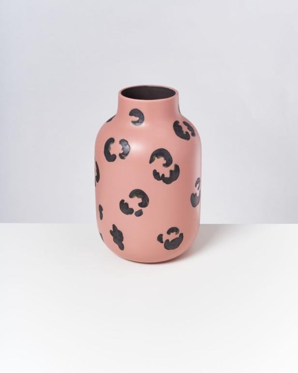 Eine rosa Vase mit schwarzem Leopardenmuster steht auf einem weißen Tisch.