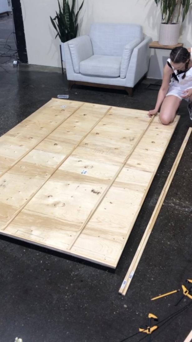 Eine Frau kniet neben einer großen Holzplatte, die aus mehreren Brettern zusammengesetzt ist.
