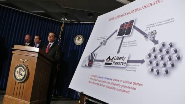 Drei Männer stehen an einem Rednerpult mit einem Diagramm über Liberty Reserve im Hintergrund.