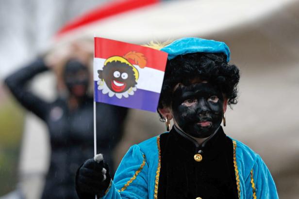 Eine Person mit schwarzer Schminke hält eine Flagge mit einer Cartoon-Figur.
