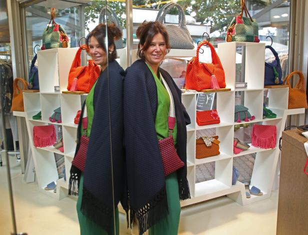 Eine Frau posiert vor einem Regal mit handgefertigten Taschen und Accessoires.