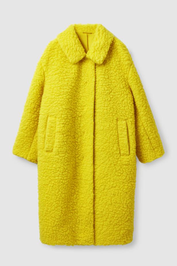 Ein gelber Teddyfellmantel mit Kragen und Taschen vor einem grauen Hintergrund.