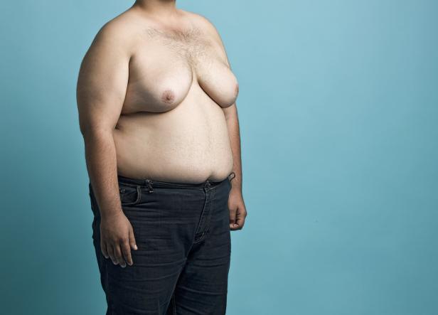 Ein Mann mit nacktem Oberkörper und Jeans steht vor einem türkisfarbenen Hintergrund.