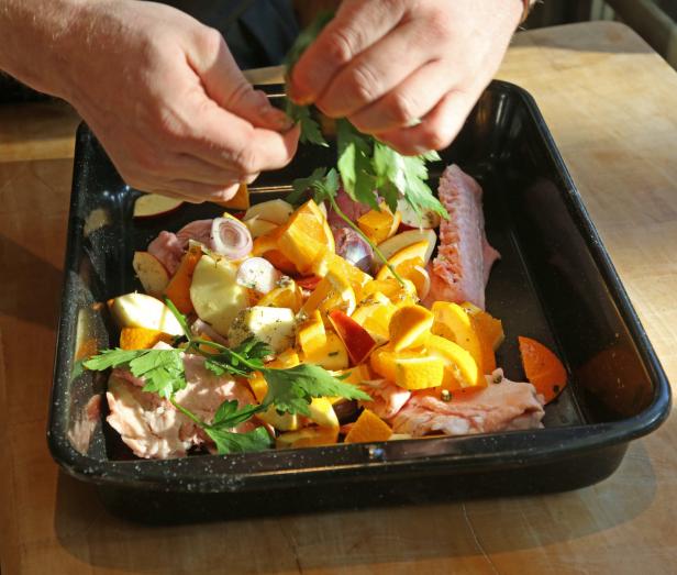 Hände garnieren Schweinefleisch mit Orangen, Äpfeln und Kräutern in einer schwarzen Pfanne.